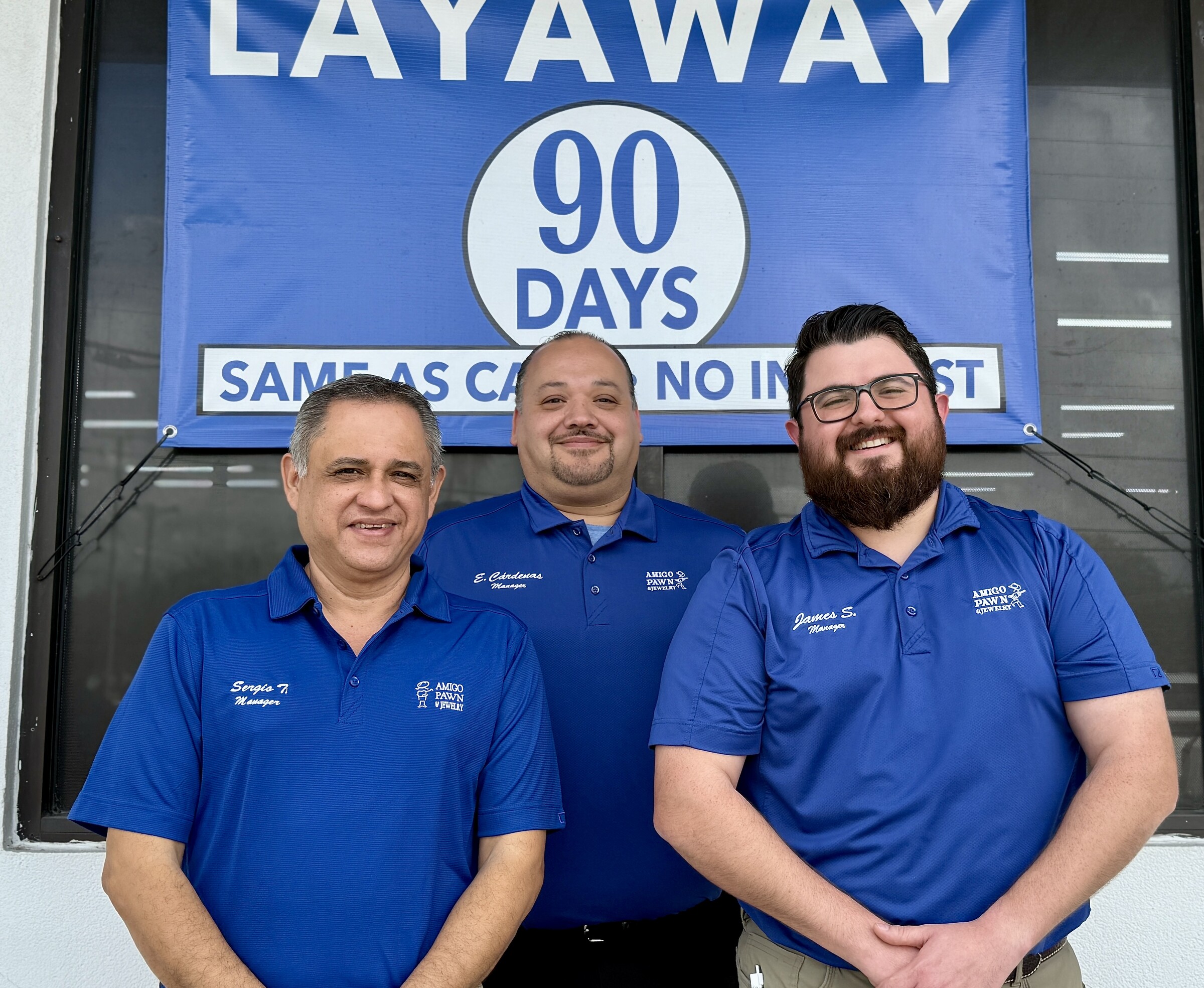 Three Amigo managers posing in front of a layaway banner